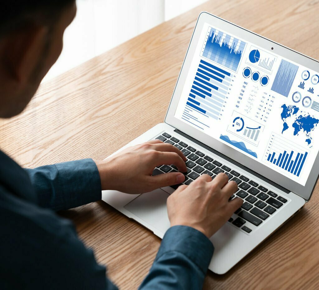 Man types on laptop. Only his profile and hands are visible. The laptop screen has charts and graphs as he works for data infrastructure and data culture.